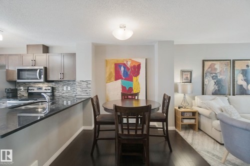 Kitchen featuring dark cabinetry, stainless steel appliances, a multi-tone tile backsplash, and dark countertops - #58 4029 Orchards Dr Sw, Edmonton, AB 