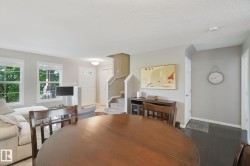 Spacious living area featuring light-toned walls, dark wood-finish flooring, and multiple windows - 
