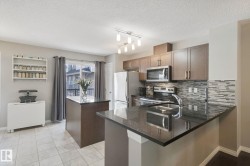 Kitchen featuring dark wood-finish cabinetry, stainless steel appliances, a tile backsplash, dark countertops, and tile flooring - 