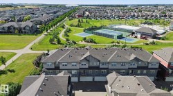 Multi-unit residential structures with attached garages, surrounded by extensive green spaces, paved pathways, and recreational courts - 