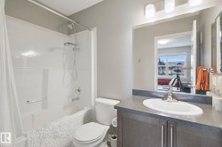 Integrated bathtub and shower with white panel surround, brushed nickel fixtures, gray vanity with undermount sink, and three-light vanity bar - 