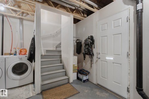 Laundry area featuring a front-loading washing machine, adjacent to a staircase with a handrail - #58 4029 Orchards Dr Sw, Edmonton, AB 