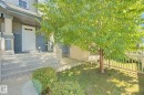 Exterior featuring blue siding, a white entry door with upper window panes, concrete steps, a partial white picket fence, and mature landscaping - #58 4029 Orchards Dr Sw, Edmonton, AB 