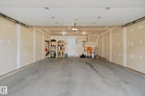 Spacious garage featuring a concrete floor, exposed framing, and an interior access door - #58 4029 Orchards Dr Sw, Edmonton, AB 