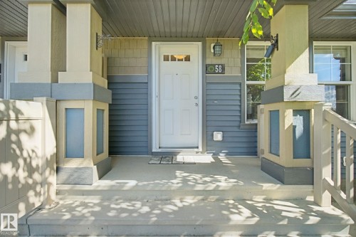 Covered concrete front porch with architectural columns, horizontal siding, and a white entry door with frosted glass - #58 4029 Orchards Dr Sw, Edmonton, AB 