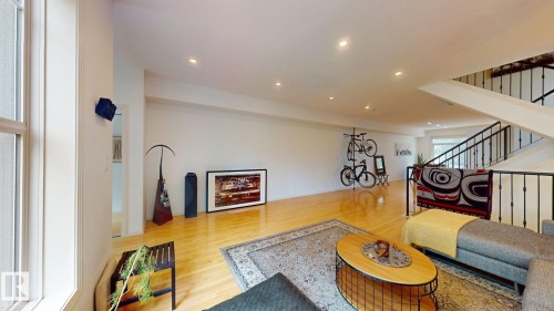 Expansive open-concept room featuring light wood flooring, recessed lighting, and a prominent staircase with metal railings - 9846 112 Street Nw, Edmonton, AB 