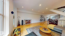 Expansive open-concept room featuring light wood flooring, recessed lighting, and a prominent staircase with metal railings - 