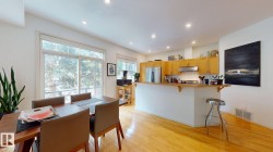Open-concept living space with wood-finish flooring, recessed lighting, expansive glass sliding doors, and a kitchen featuring wood cabinetry, stainless steel appliances, and a breakfast bar - 