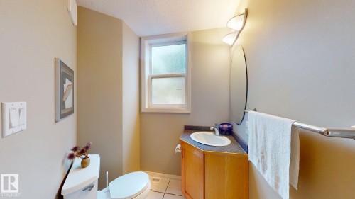 Bathroom featuring a window, built-in vanity with wood-finish cabinetry, countertop with an integrated sink, wall-mounted mirror, and tile flooring - 9846 112 Street Nw, Edmonton, AB 