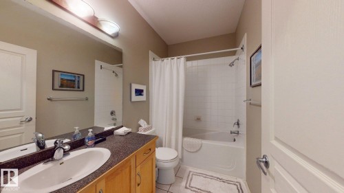 Bathroom featuring a wood-finish vanity with an integrated sink, dark speckled countertop, and a full-width mirror - 9846 112 Street Nw, Edmonton, AB 