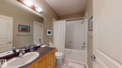 Bathroom featuring a wood-finish vanity with an integrated sink, dark speckled countertop, and a full-width mirror - 