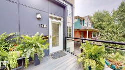 Modern exterior siding with a prominent entry door, contemporary outdoor lighting, a full-lite storm door, and a wood-finish balcony deck with black railing - 