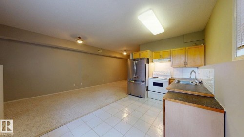 Kitchen area with wood-finish cabinetry, stainless steel refrigerator, white tile backsplash, and a sink with a gooseneck faucet - 9846 112 Street Nw, Edmonton, AB 