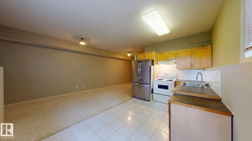 Kitchenette with wood-finish cabinetry, stainless steel refrigerator, electric range, and tile flooring - 9846 112 Street Nw, Edmonton, AB 