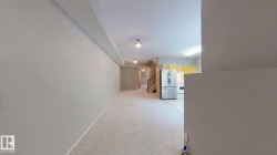 Open-concept living space with textured carpeting, a kitchen featuring stainless steel appliances, and wood-finish stair railings - 