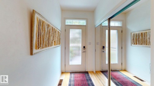 Entryway featuring wood-finish flooring, a full-length mirrored closet, and a frosted glass door with transom window - 9846 112 Street Nw, Edmonton, AB 