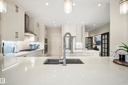 Gourmet kitchen featuring a large island with an undermount sink and pull-down faucet, light-colored cabinetry, stainless steel appliances, a gas range with a range hood, and recessed lighting - 5966 Edmonds Crescent Nw, Edmonton, AB - Indoor Photo Showing Kitchen With Double Sink With Upgraded Kitchen