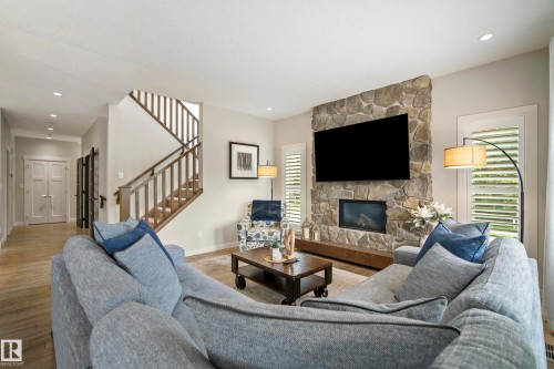 Living area featuring a stone accent wall with an integrated fireplace and television, wood-finish flooring, recessed lighting, and plantation shutters - 5966 Edmonds Crescent Nw, Edmonton, AB - Indoor Photo Showing Living Room With Fireplace