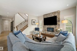 Living area featuring a stone accent wall with an integrated fireplace and television, wood-finish flooring, recessed lighting, and plantation shutters - 