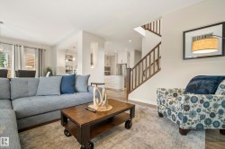 Spacious living area featuring wood-finish flooring, a contemporary staircase with wood railings, recessed lighting, and a kitchen with white cabinetry and stainless steel appliances - 