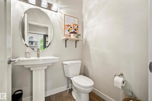 Pedestal sink with an oval frameless mirror, complemented by a three-light vanity fixture - 5966 Edmonds Crescent Nw, Edmonton, AB - Indoor Photo Showing Bathroom