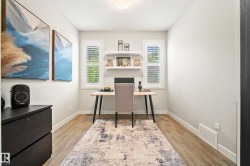 Dedicated office space featuring wood-finish flooring, two large windows with plantation shutters, recessed lighting, and wall-mounted shelving - 