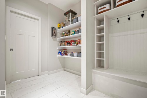 Pantry and mudroom area featuring white plank shelving, built-in bench with beadboard paneling, black coat hooks, and light rectangular floor tiles - 5966 Edmonds Crescent Nw, Edmonton, AB - Indoor