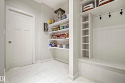 Pantry and mudroom area featuring white plank shelving, built-in bench with beadboard paneling, black coat hooks, and light rectangular floor tiles - 