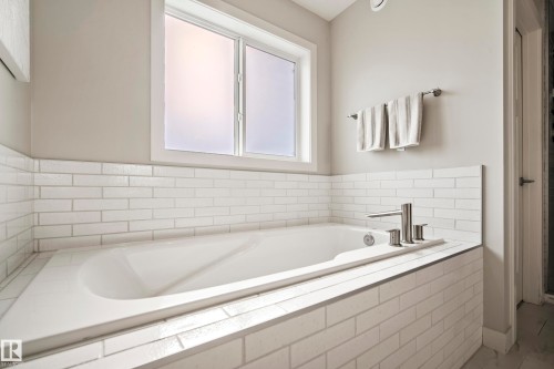 Built-in soaking tub featuring white subway tile surround, a frosted window, and brushed nickel fixtures - 5966 Edmonds Crescent Nw, Edmonton, AB - Indoor Photo Showing Bathroom