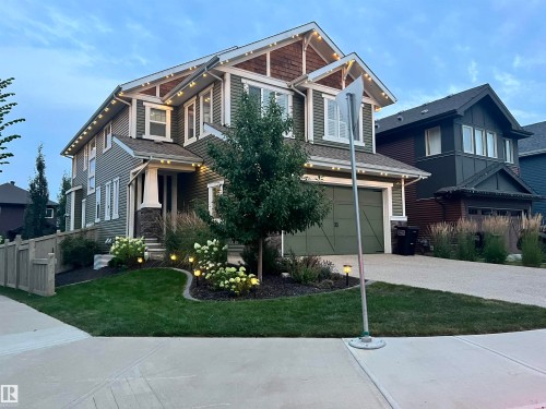Two-story residence featuring green siding with white trim, a covered entry porch with stone accents, a two-car garage, and established landscaping with accent lighting - 5966 Edmonds Crescent Nw, Edmonton, AB - Outdoor With Facade