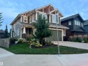 Two-story residence featuring green siding with white trim, a covered entry porch with stone accents, a two-car garage, and established landscaping with accent lighting - 5966 Edmonds Crescent Nw, Edmonton, AB  - Outdoor With Facade 