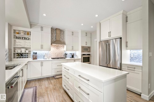 Kitchen featuring a central island with countertop, extensive white cabinetry, stainless steel appliances, a decorative tiled backsplash, and wood-finish flooring - 5966 Edmonds Crescent Nw, Edmonton, AB - Indoor Photo Showing Kitchen With Upgraded Kitchen