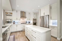 Kitchen featuring a central island with countertop, extensive white cabinetry, stainless steel appliances, a decorative tiled backsplash, and wood-finish flooring - 