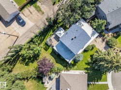 Aerial view of a contemporary home featuring a newly installed asphalt shingle roof, expansive manicured lawn, and mature landscaping with established trees throughout the property - 