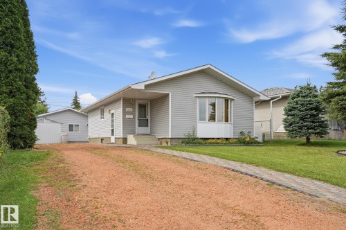 Light grey siding exterior featuring a prominent bay window, a concrete entry with a storm door, and a gravel driveway - 13304 63 Street Nw, Edmonton, AB 