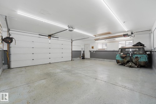 Spacious garage featuring a sectional overhead door, concrete flooring, linear ceiling lighting, and built-in shelving - 13304 63 Street Nw, Edmonton, AB 