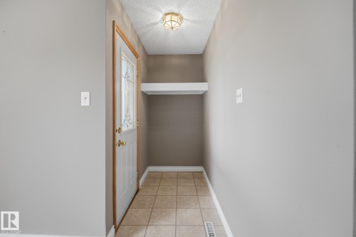 Tiled flooring entryway with a white door, decorative glass insert, and brass hardware - 13304 63 Street Nw, Edmonton, AB 