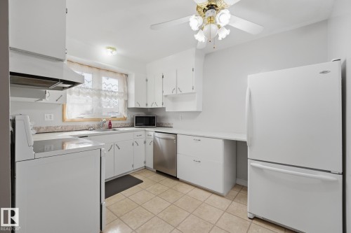 Kitchen featuring white cabinetry, a built-in dishwasher, tile flooring, and a ceiling fan with integrated lighting - 13304 63 Street Nw, Edmonton, AB 