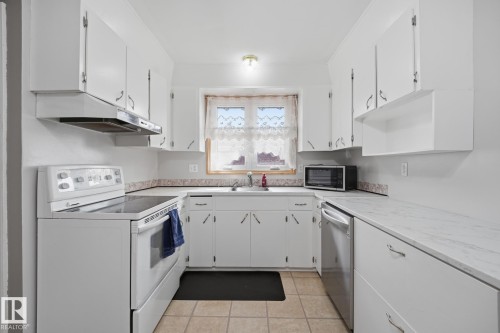 Kitchen featuring white cabinetry, tile flooring, and a stainless steel dishwasher - 13304 63 Street Nw, Edmonton, AB 