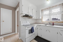 Kitchen featuring white cabinetry, a built-in range hood, a stainless steel sink, and light-colored tile flooring - 