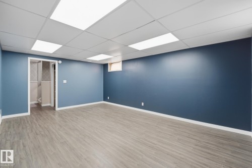 Spacious room with blue-painted walls, wood-finish flooring, and a drop ceiling with integrated lighting - 13304 63 Street Nw, Edmonton, AB 