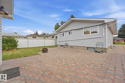 Exterior featuring gray siding, multiple windows, a white privacy fence, an expansive paver patio, and a manicured lawn - 13304 63 Street Nw, Edmonton, AB 