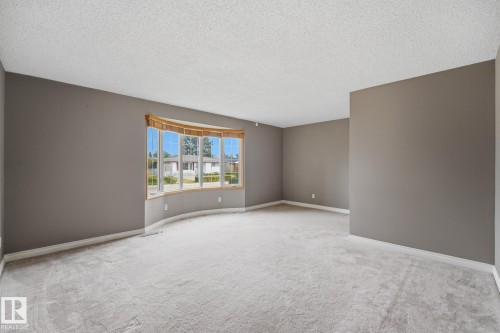 Spacious interior featuring a large bay window with wood trim, neutral wall color, and light-toned carpeting - 13304 63 Street Nw, Edmonton, AB 