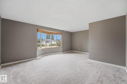 Spacious interior featuring a large bay window with wood trim, neutral wall color, and light-toned carpeting - 