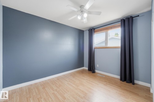Room featuring wood-finish flooring, a ceiling fan with integrated lighting, and a window with wood trim - 13304 63 Street Nw, Edmonton, AB 