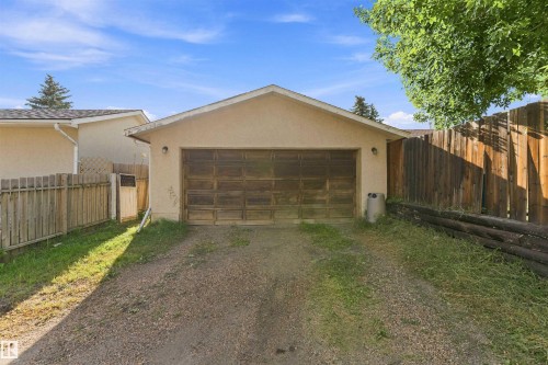 Detached garage with a paneled door and exterior light fixture, accompanied by a gravel driveway, wood fencing, and a side gate - 17005 95 Street Nw, Edmonton, AB 