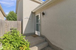 Stucco exterior with a prominent address number, featuring an exterior wall-mounted light fixture, and a front entry door with a storm door - 