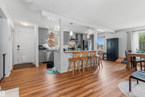 Wood-finish flooring throughout, kitchen with gray cabinetry, stainless steel appliances, stone countertops, and a dining area - 17005 95 Street Nw, Edmonton, AB 