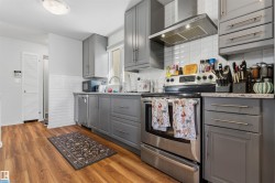 Wood-finish flooring with a modern kitchen featuring gray cabinetry, stainless steel appliances, white subway tile backsplash, and light-toned countertops - 
