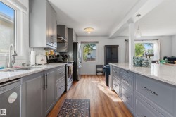 Kitchen featuring gray cabinetry, light-toned countertops, wood-finish flooring, a stainless steel sink, and white subway tile backsplash - 
